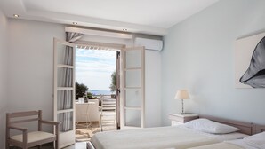 A hotel room with two beds, a chair, a desk, and an open door leading to a balcony with a view. - Kavuras Village Hotel & Suites (Naxos)