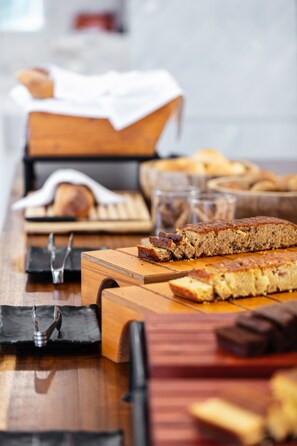 A wooden table with various baked goods, including bread and cakes, and a knife. - Kavuras Village Hotel & Suites (Naxos)
