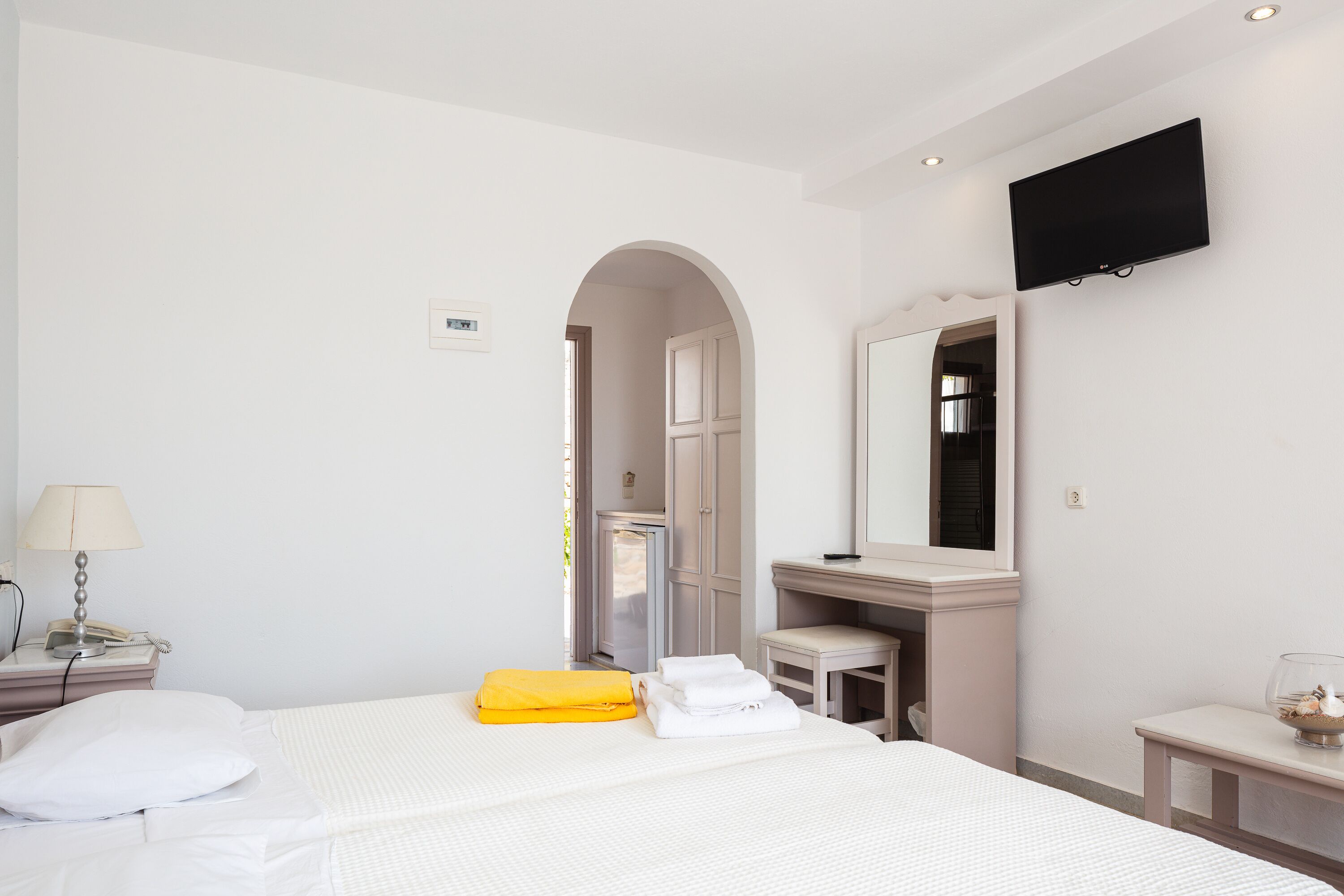 A hotel room with a bed, a desk, a chair, a TV, and a bathroom visible through an archway.
