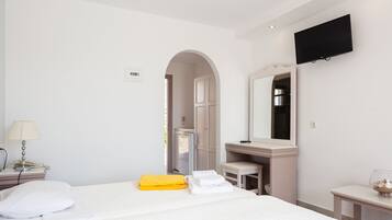 A hotel room with a bed, a desk, a chair, a TV, and a bathroom visible through an archway.