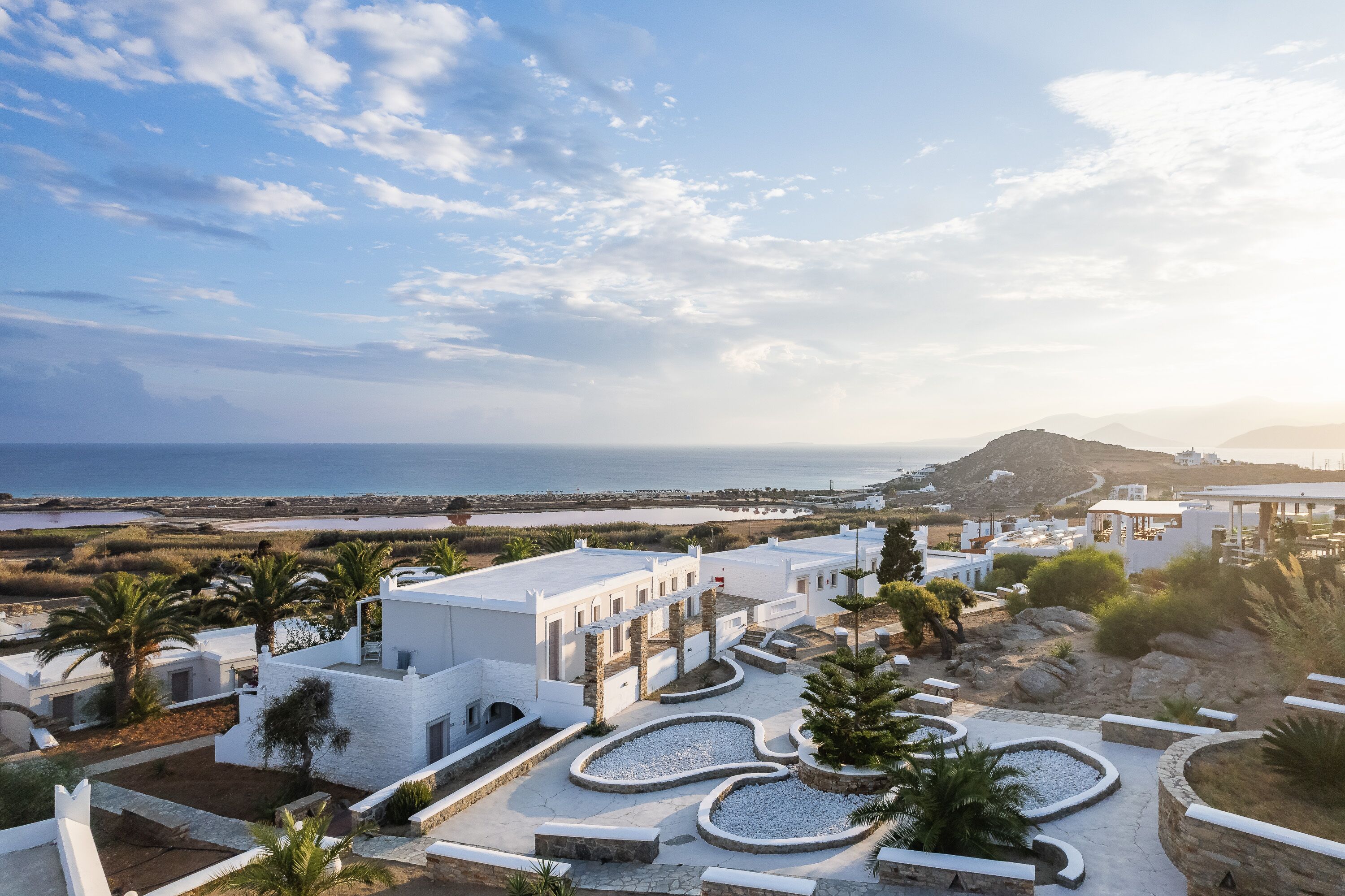 A coastal resort with white buildings, palm trees, and a view of the sea and mountains.