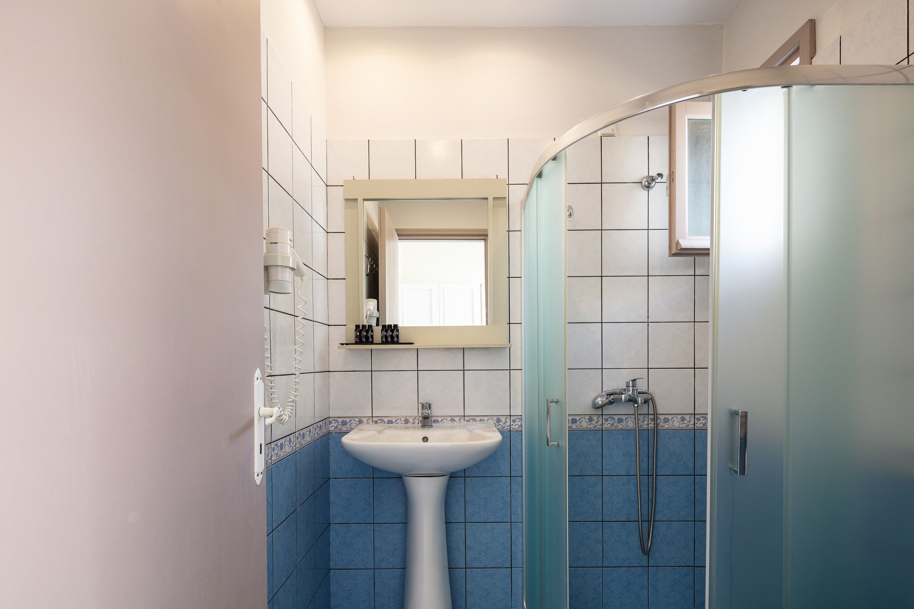 Un baño con lavamanos pedestal, cabina de ducha de vidrio y espejo sobre el lavamanos.