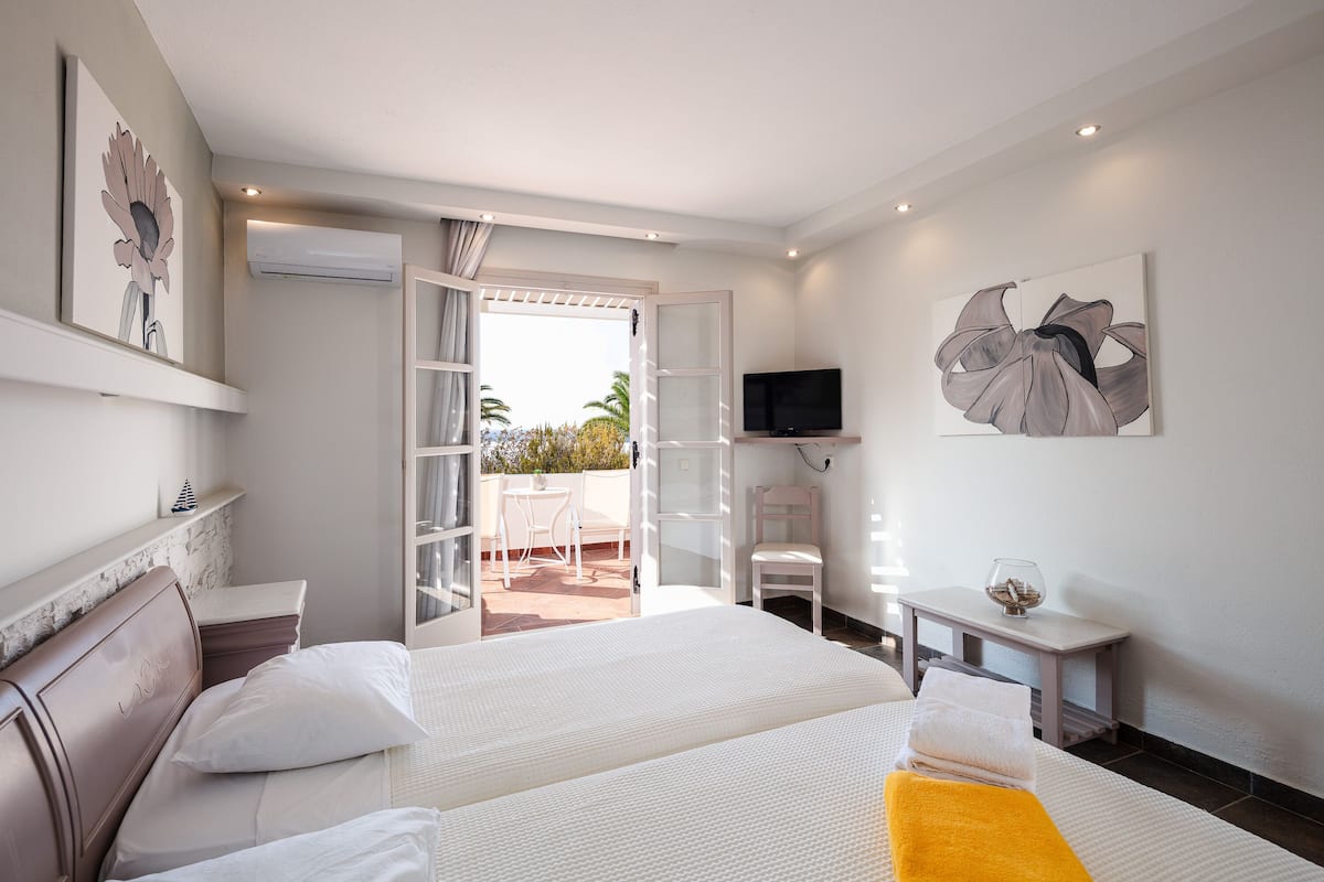 A hotel room with two beds, a TV, a small table with a glass, and artwork on the walls.
