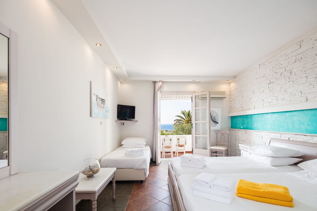 A hotel room with two beds, a TV, a balcony with a view, and a white brick wall.