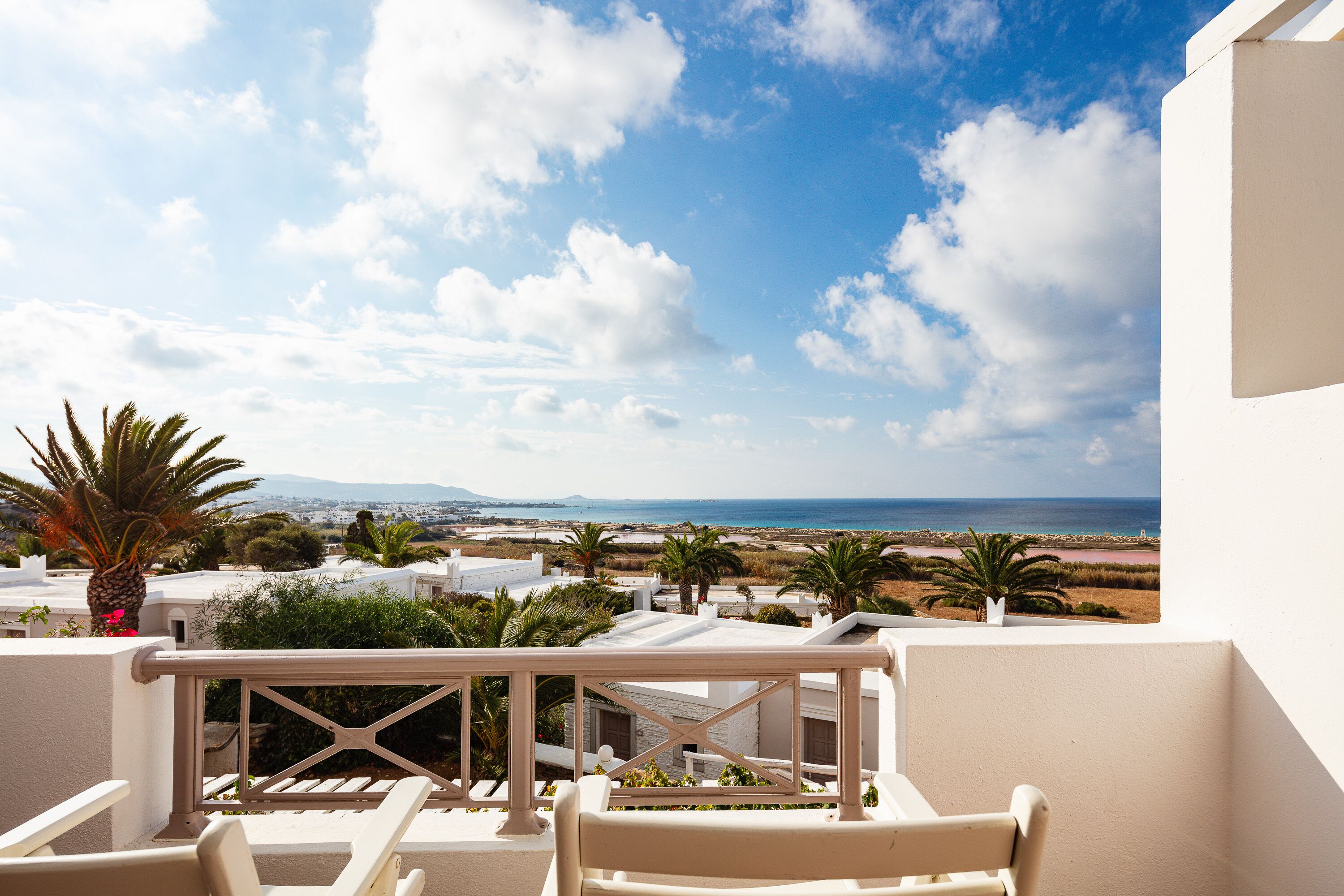 A balcony with white furniture, a view of the sea, and a clear sky.