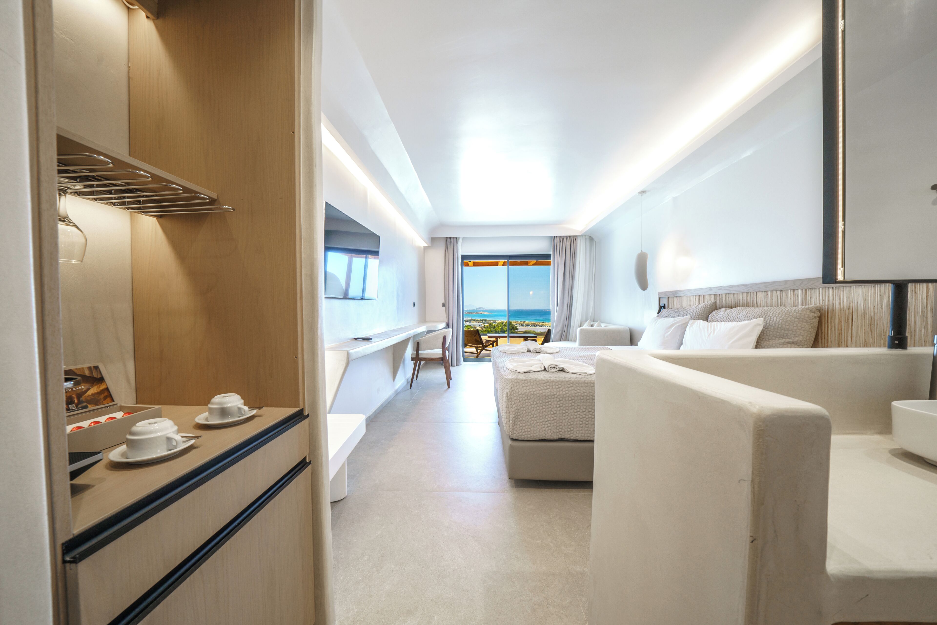 A modern hotel room with a balcony, a seating area, and a view of the sea.