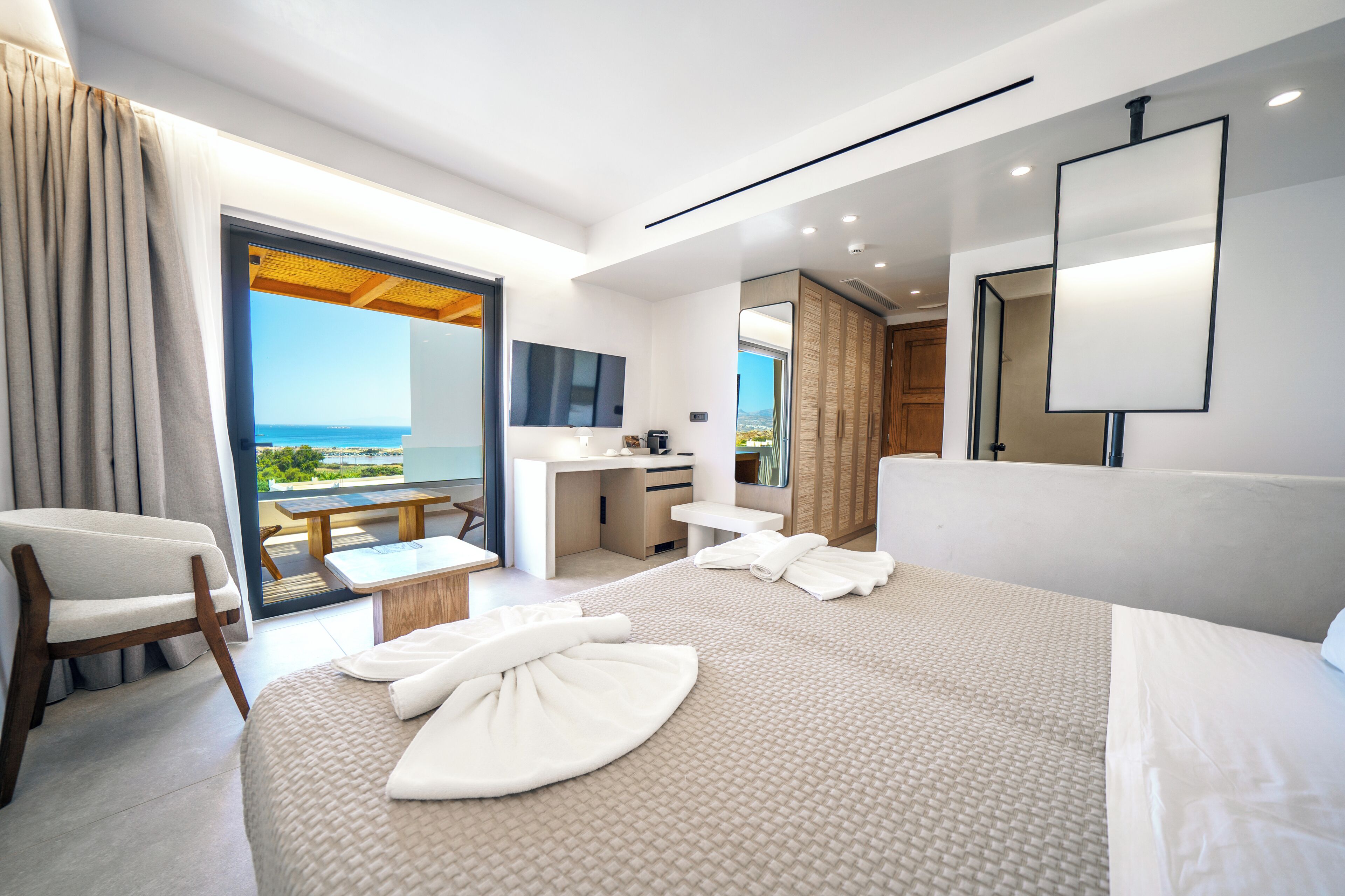A modern hotel room with a large bed, a sitting area, a desk, and a bathroom.