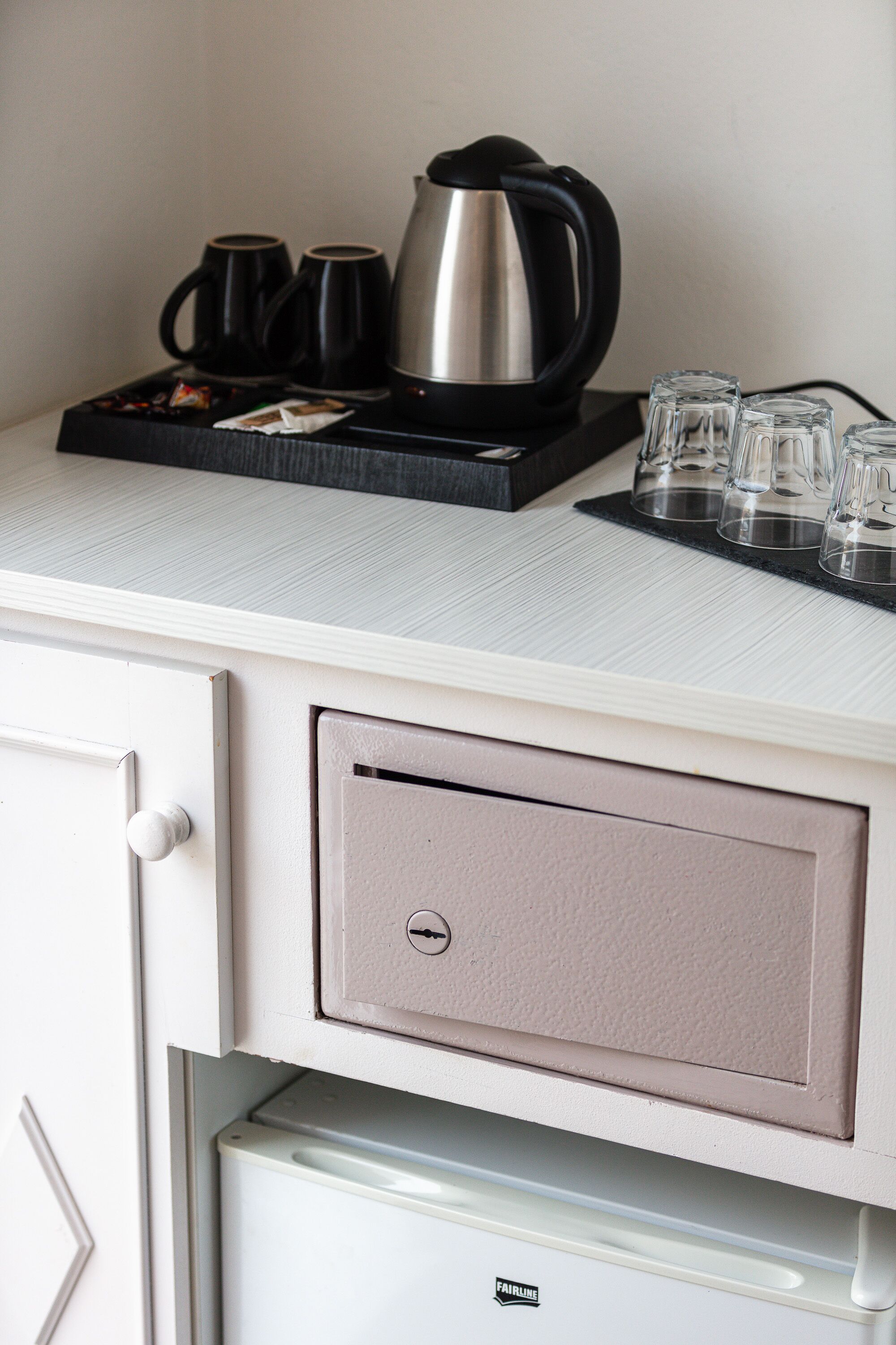 A kitchenette with a coffee maker, cups, and glasses on a tray.