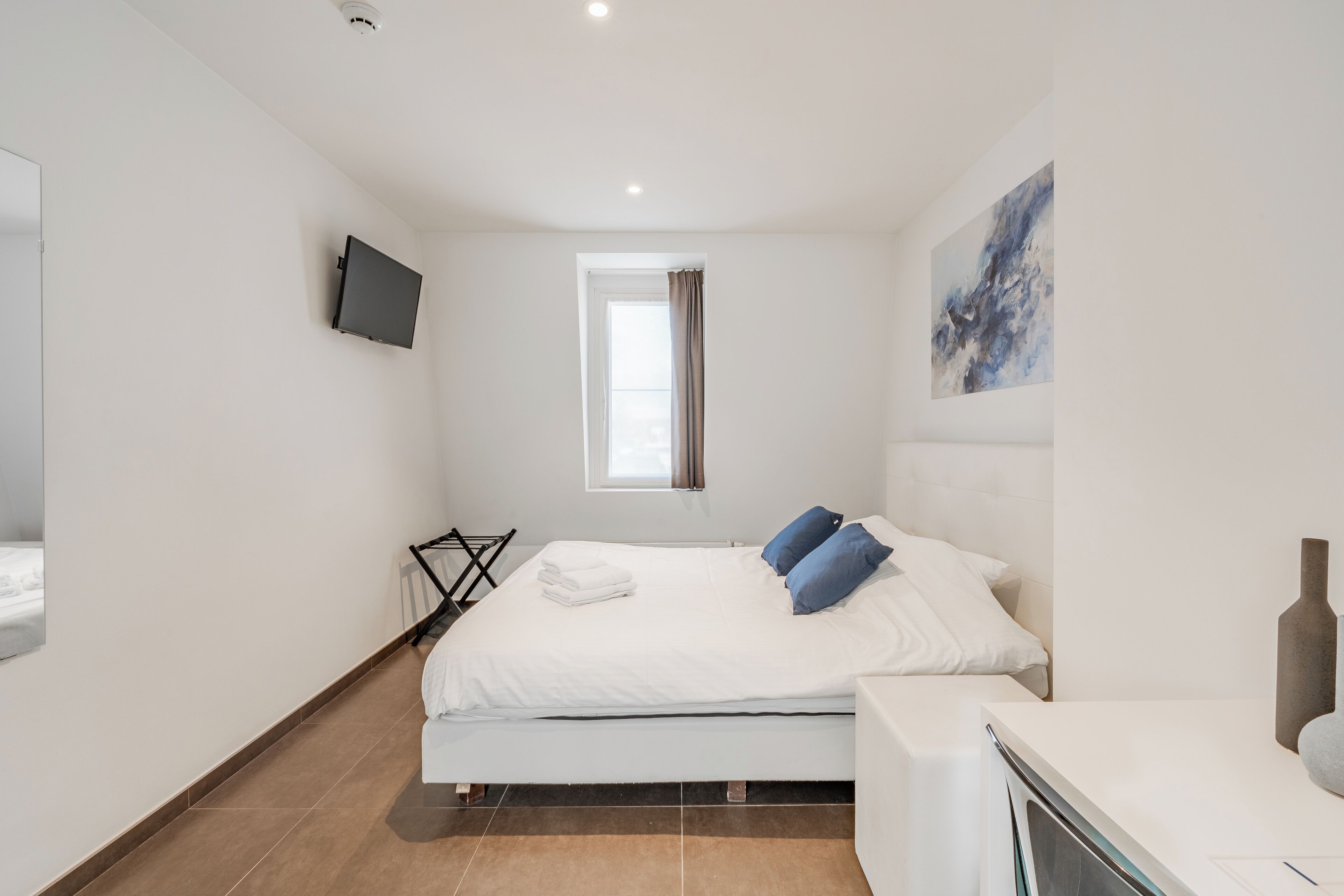 Un dormitorio moderno con cama, televisor de pantalla plana, ventana con cortinas y un cuadro en la pared.