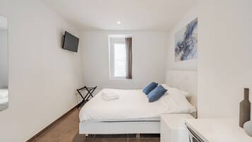 Un dormitorio moderno con cama, televisor de pantalla plana, ventana con cortinas y un cuadro en la pared.