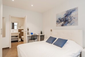 Quarto de hotel moderno com uma cama grande, uma escrivaninha e um banheiro visível através de uma porta aberta.