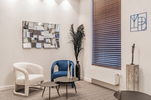 Una habitación moderna con una silla blanca y azul, una mesita pequeña y un espejo decorativo en la pared.