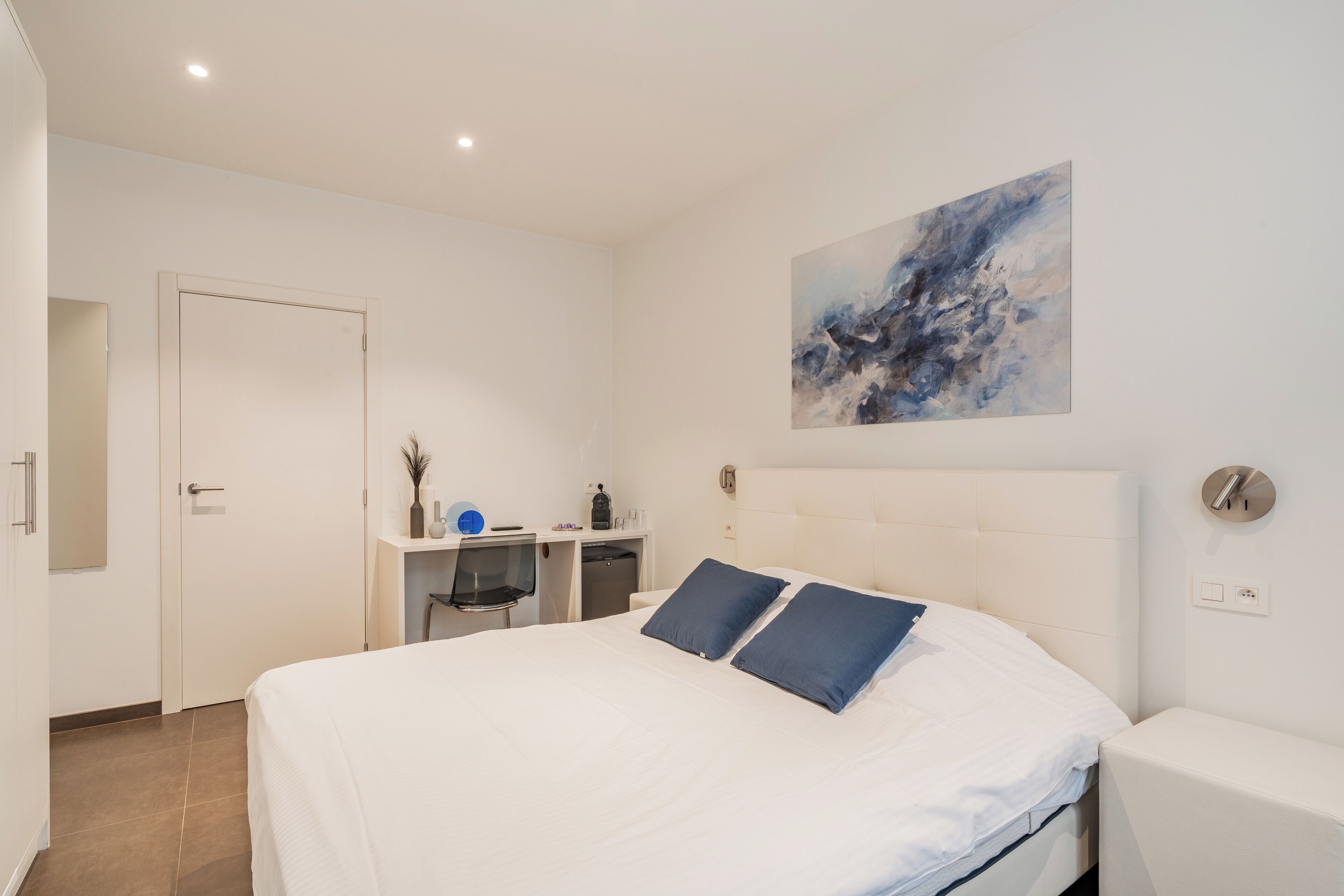 A modern bedroom with a large bed, a desk, and a chair.
