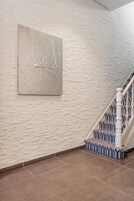Una escalera con alfombra a rayas y barandillas blancas, que conduce a un rellano con pared texturizada y un cuadro abstracto grande.