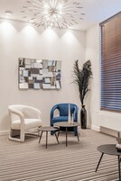 Una sala de estar moderna con un sillón blanco y azul, una mesita redonda y un espejo decorativo en la pared.