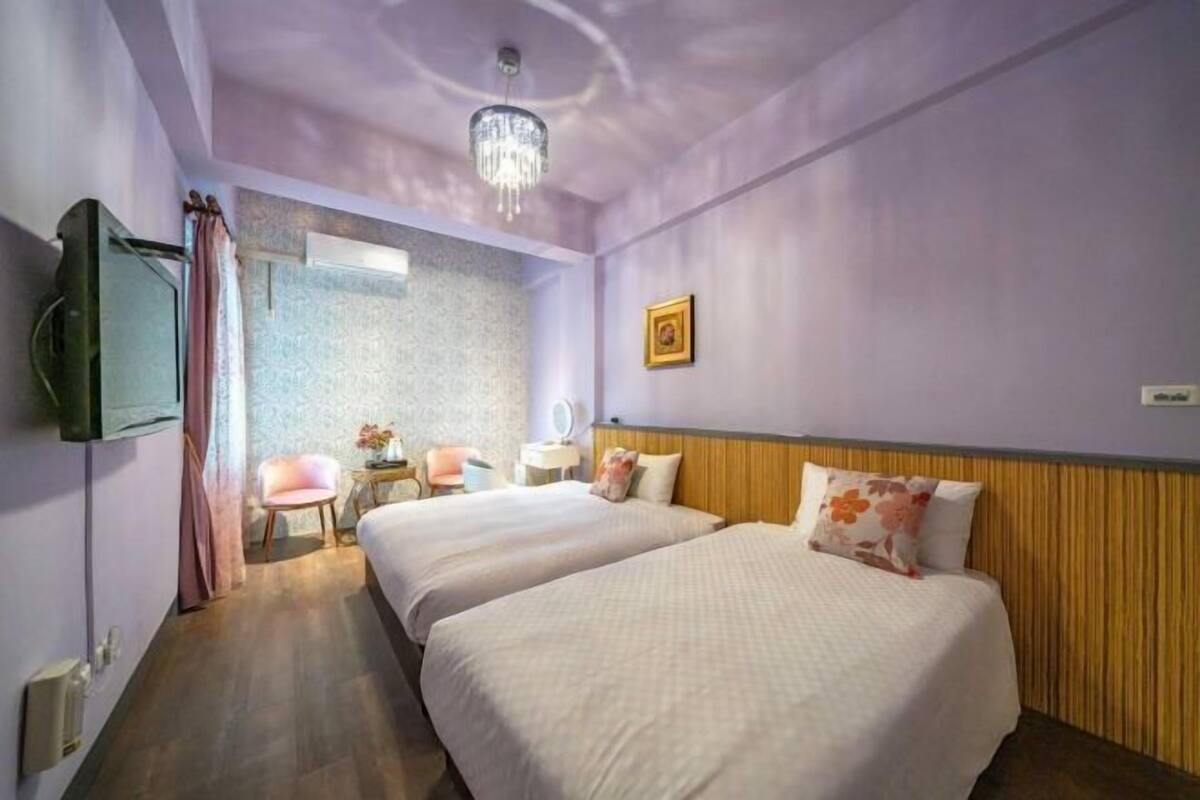 A hotel room with two beds, a chandelier, a television, and a small desk with a chair.