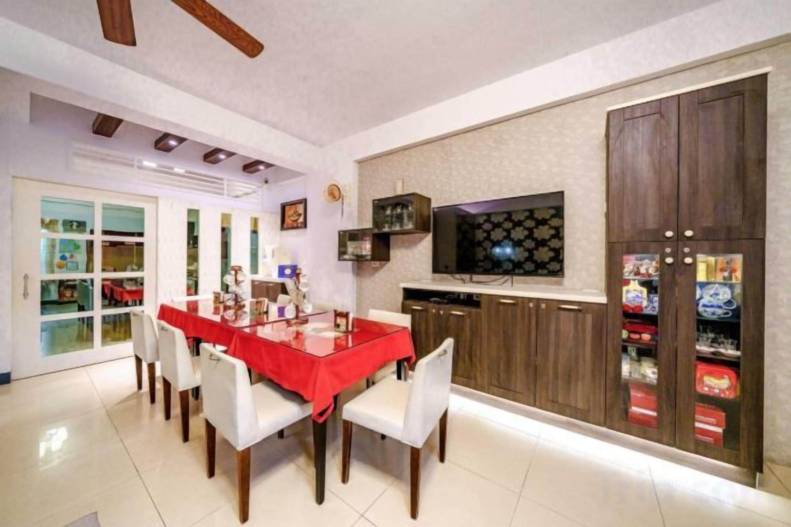 Un comedor con mantel rojo, sillas blancas y un televisor montado en la pared.