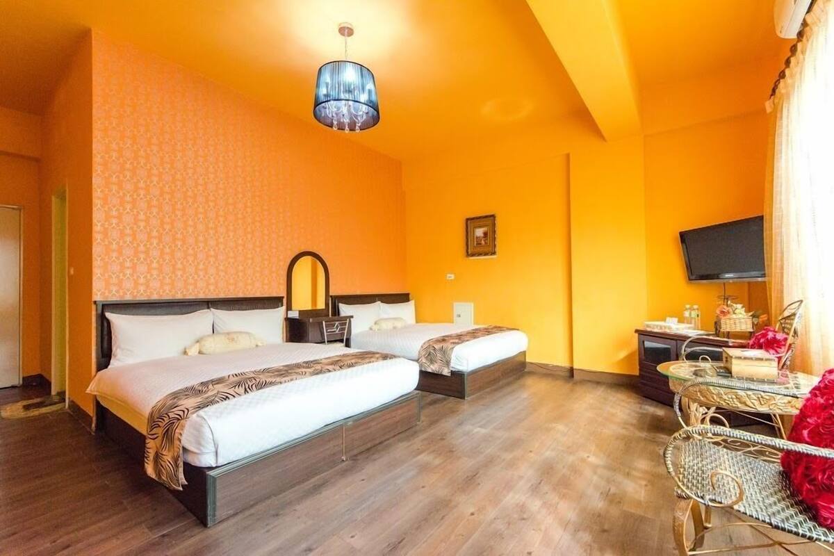 A hotel room with two beds, a television, a small table, and a wicker chair.