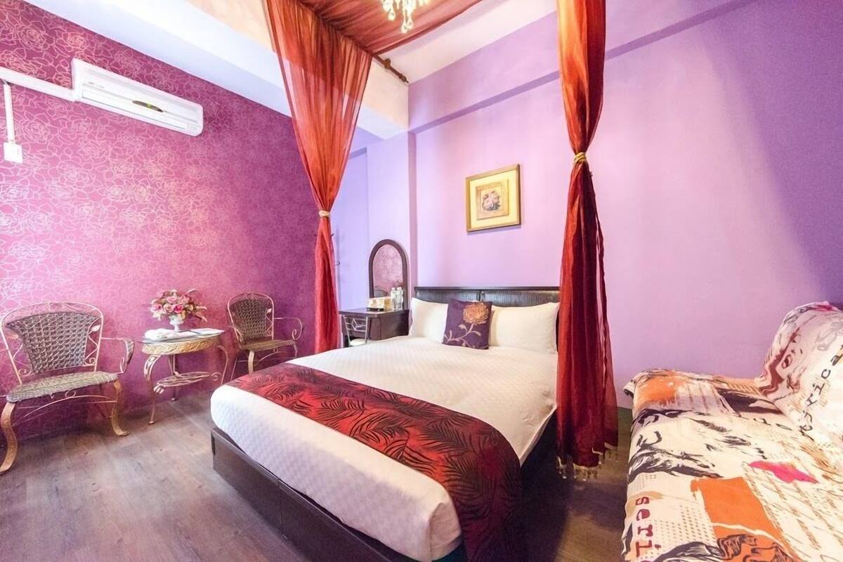 A bedroom with a large bed, two chairs, a small table, and a nightstand.