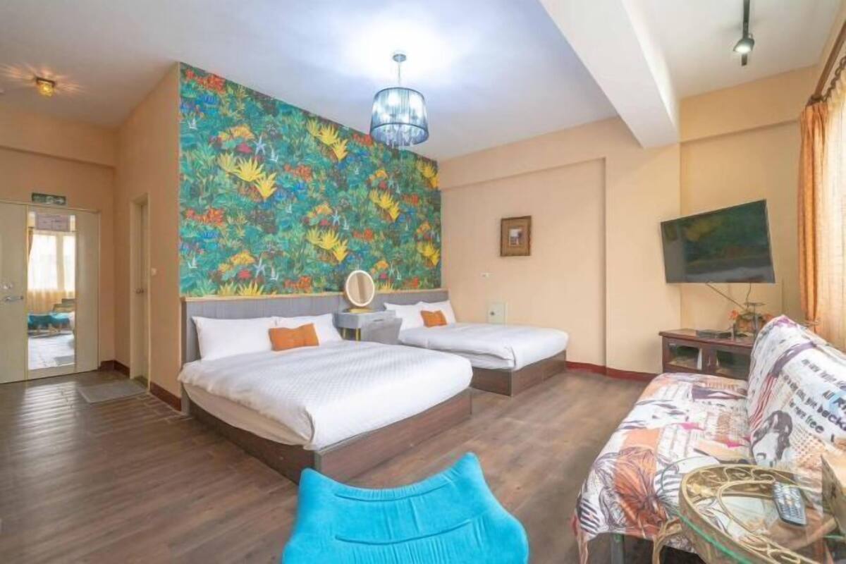 A hotel room with two beds, a colorful mural, a sofa, and a television.