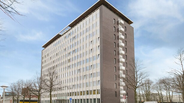 Un immeuble à plusieurs étages doté d’une architecture moderne, caractérisé par un mélange de façades en verre et en brique, et une entrée imposante avec une rampe d’accès.