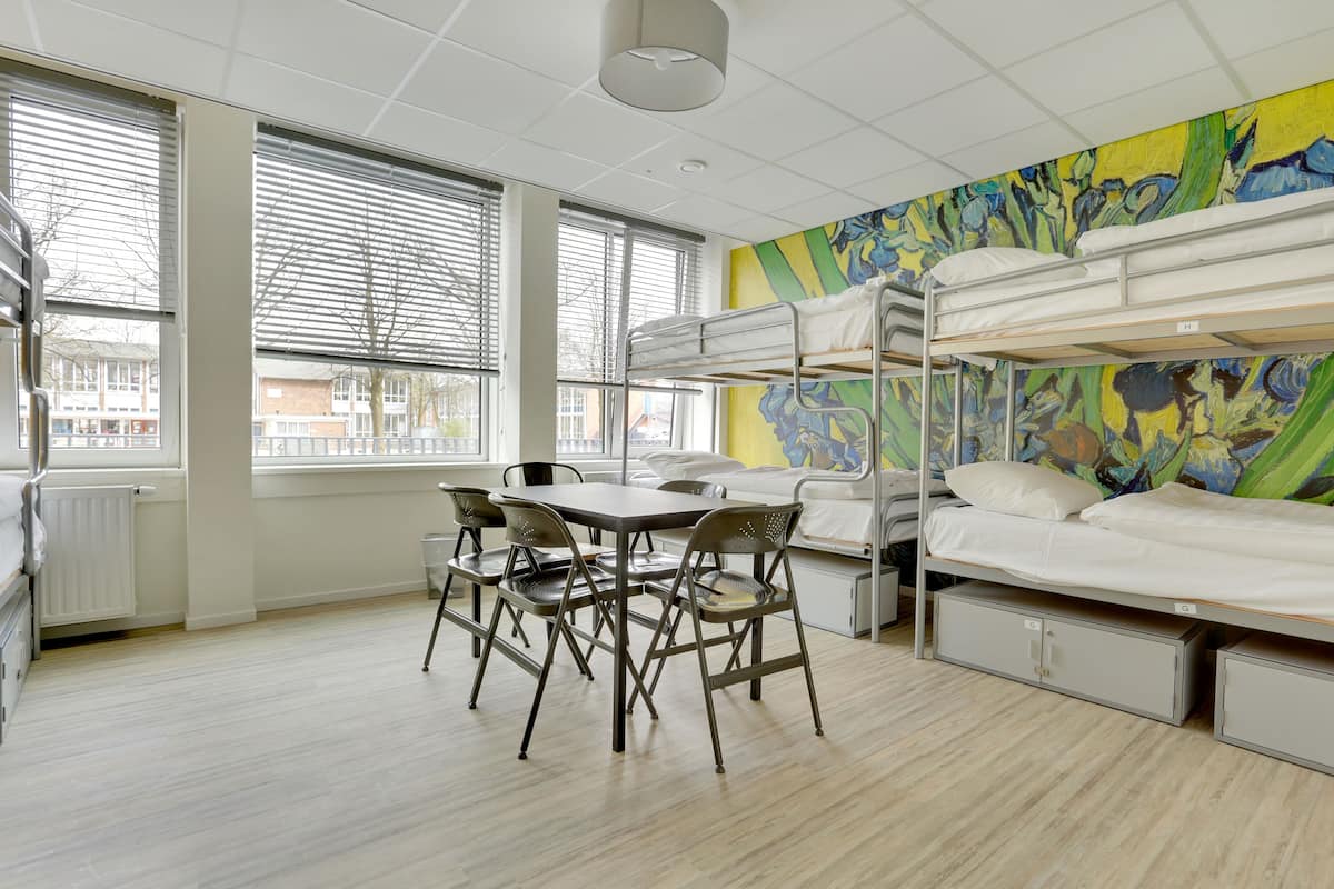 Un dormitorio con literas, una mesa con sillas y un ventanal con persianas.