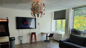 Un salon moderne avec un téléviseur à écran plat, un tabouret rouge, une table basse ronde en bois et un canapé gris.