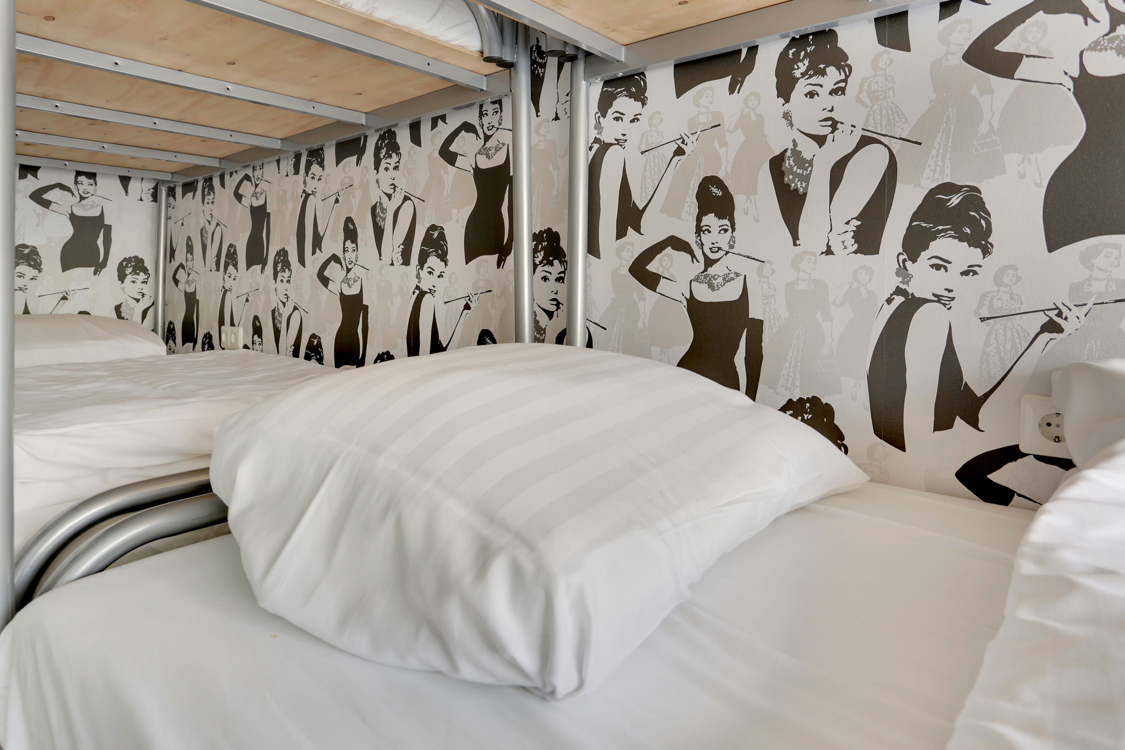 A hotel room with a bunk bed, a mural of vintage women on the wall, and a metal headboard.
