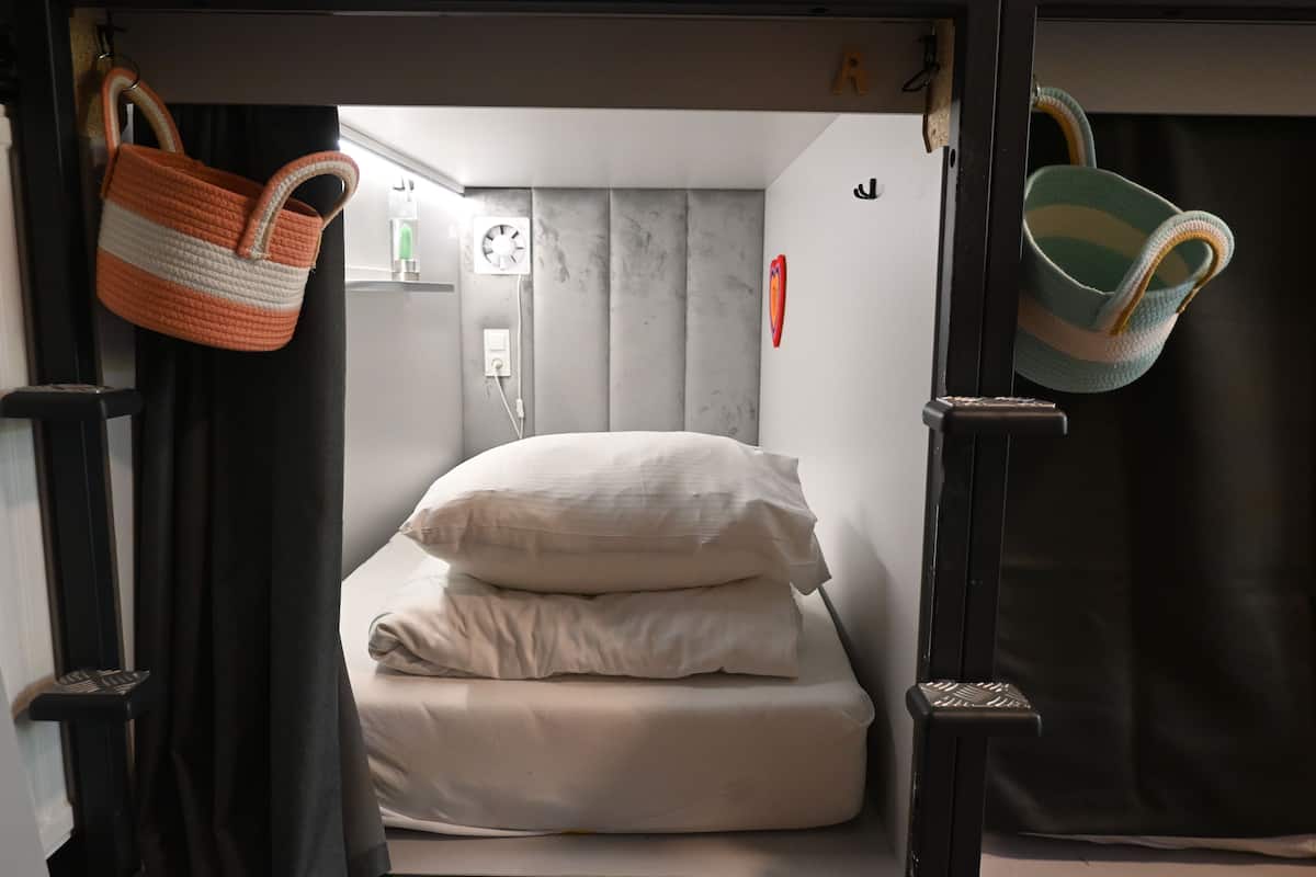 Una habitación compacta con cama, una mesita y un reloj en la pared.