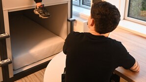 A person sitting at a table in a room with a bunk bed and a window with a view of trees. - Dutchies Hostel (Amsterdam)