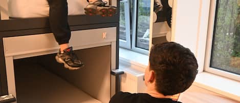 A person sitting at a table in a room with a bunk bed and a window with a view of trees.