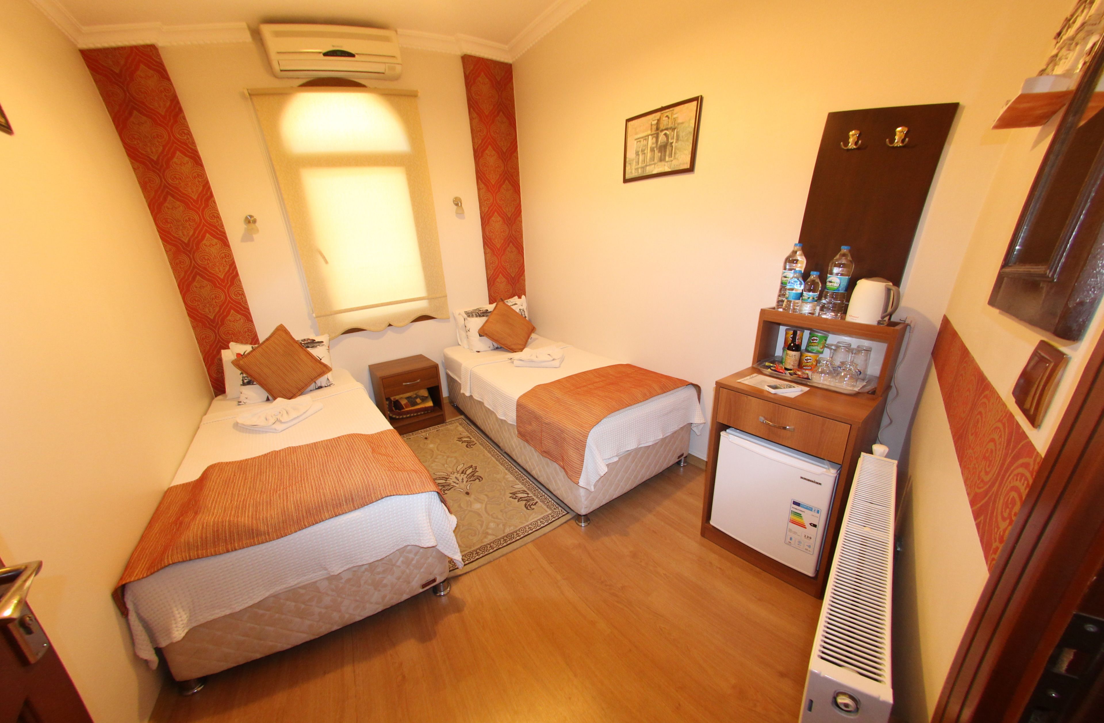 A hotel room with two beds, a small desk with a refrigerator, and a window with curtains.