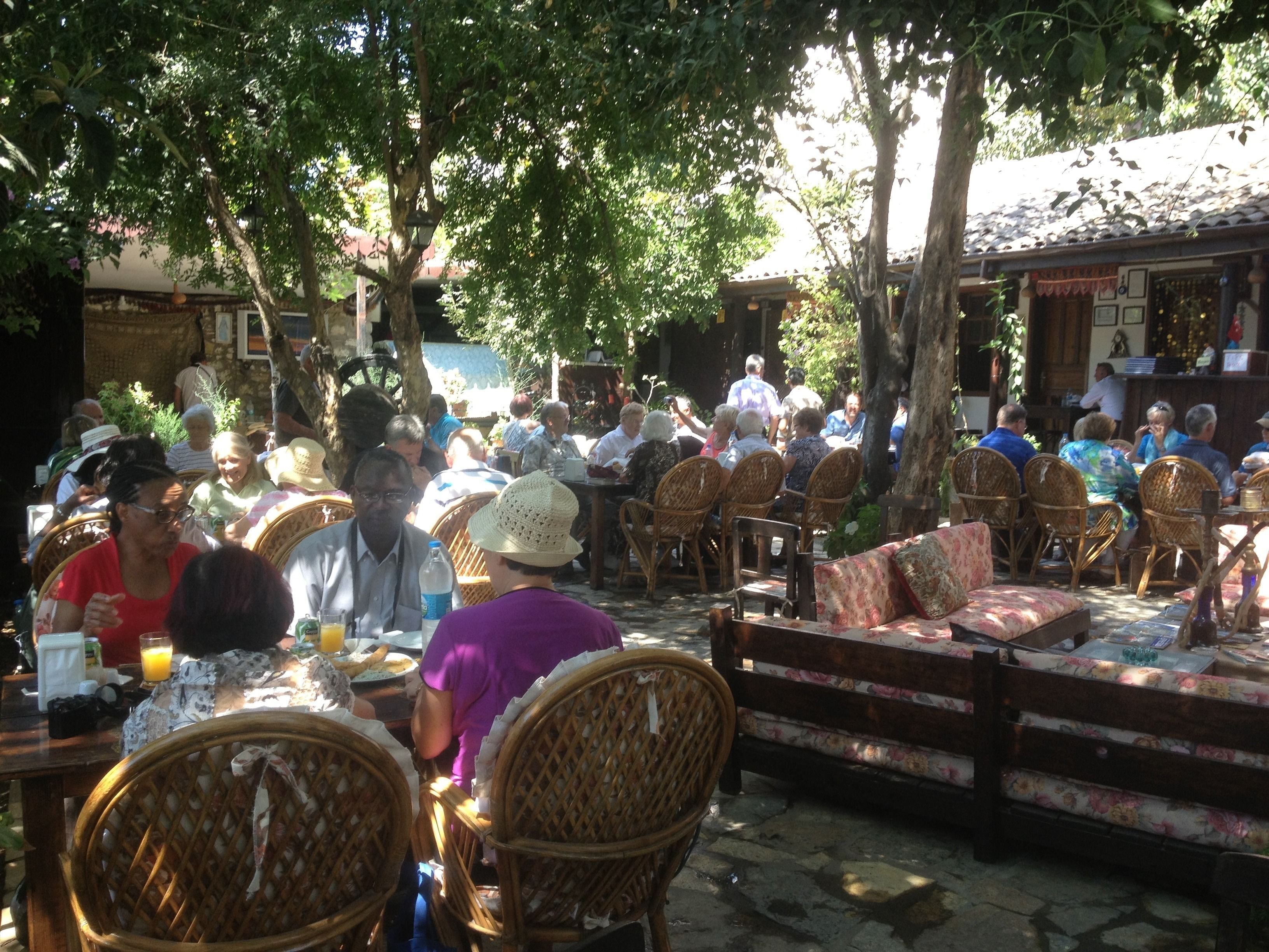 An outdoor seating area with wicker chairs and tables, surrounded by trees.
