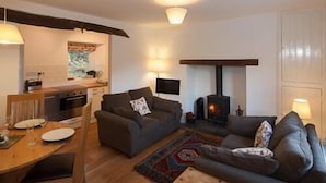 A cozy living room with a fireplace, a dining area with a table set for two, and a kitchen in the background. - Bronfelin & Troed-y-rhiw Holiday Cottages (Llanwrtyd Wells)