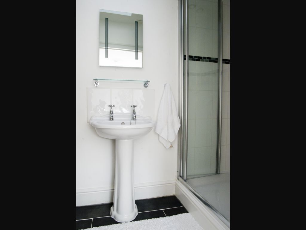 A bathroom with a pedestal sink, a glass shower enclosure, and a mirror above the sink.