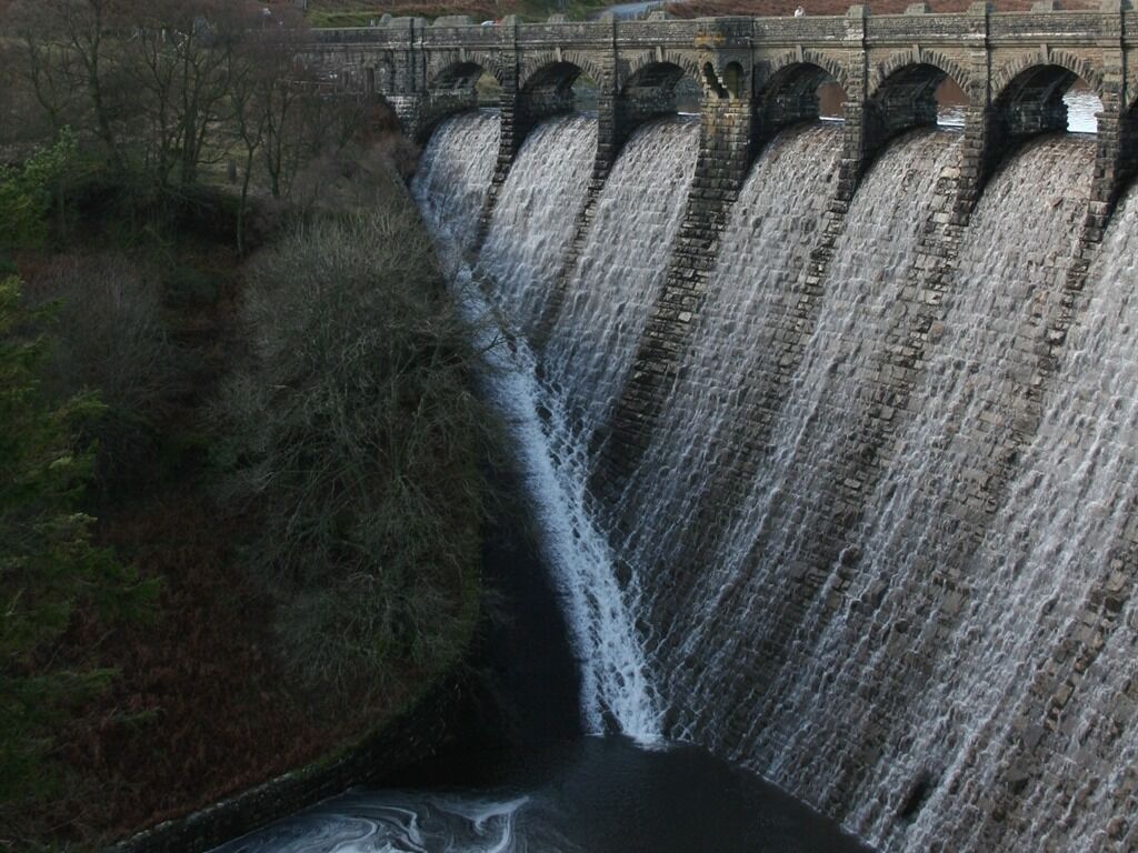 A large dam with multiple water spillways and a bridge above.