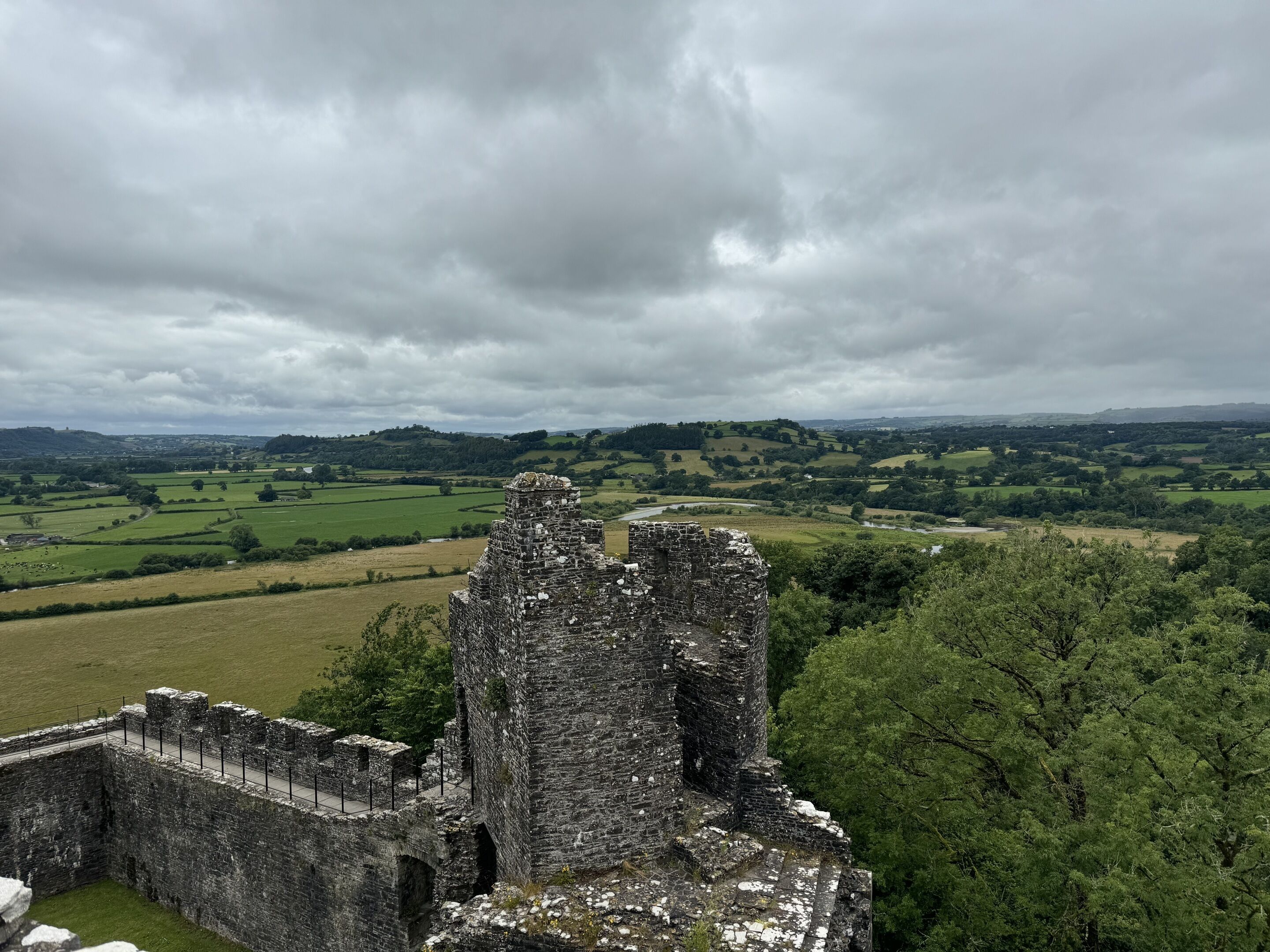 Ruínas de um castelo de pedra histórico com vista para colinas verdes ondulantes e um céu nublado.
