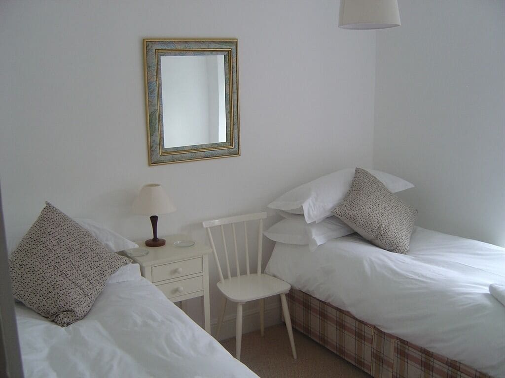 A bedroom with two beds, a chair, a bedside table, a lamp, and a mirror.
