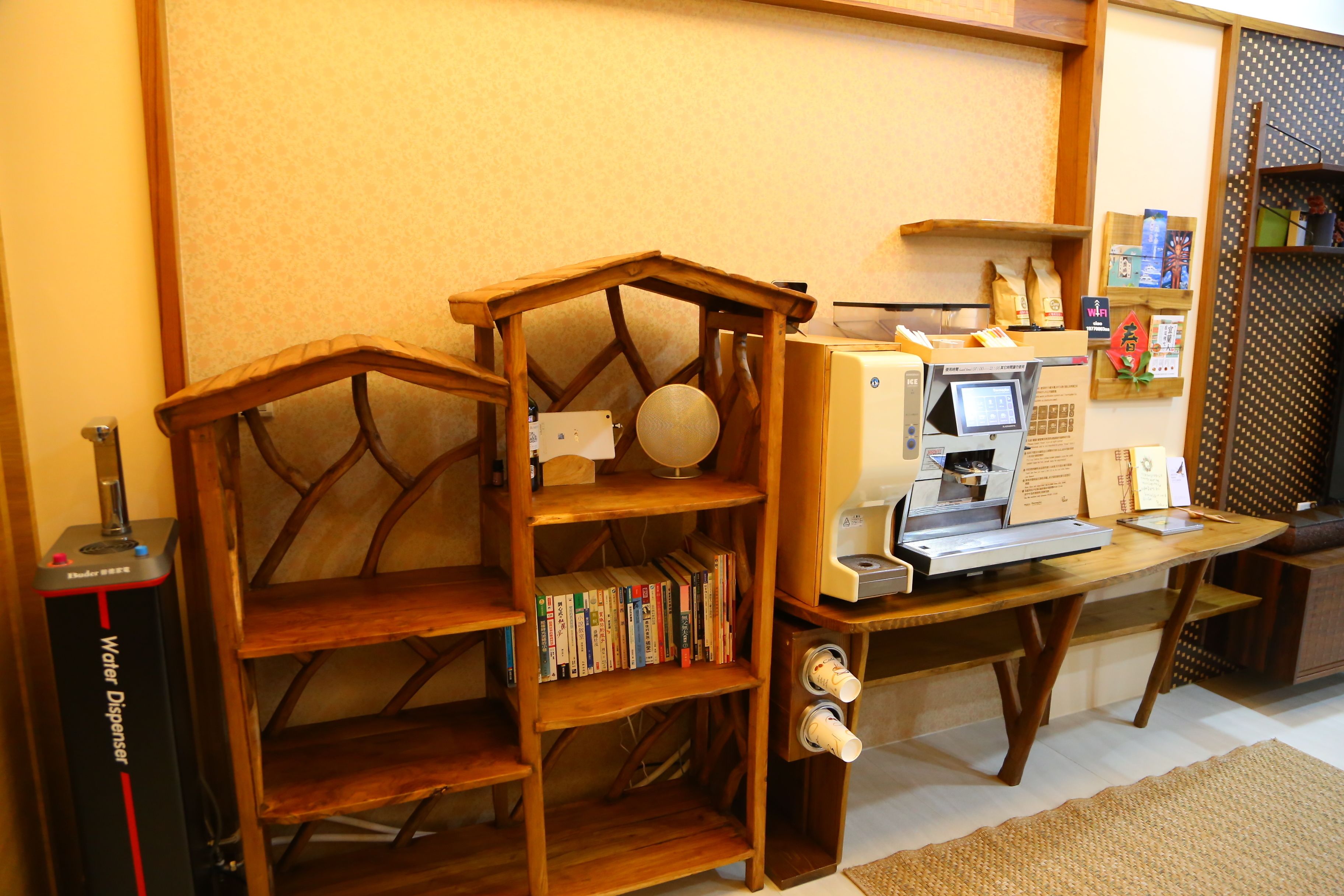 A wooden bookshelf with books, a water dispenser, and a small wooden house model.