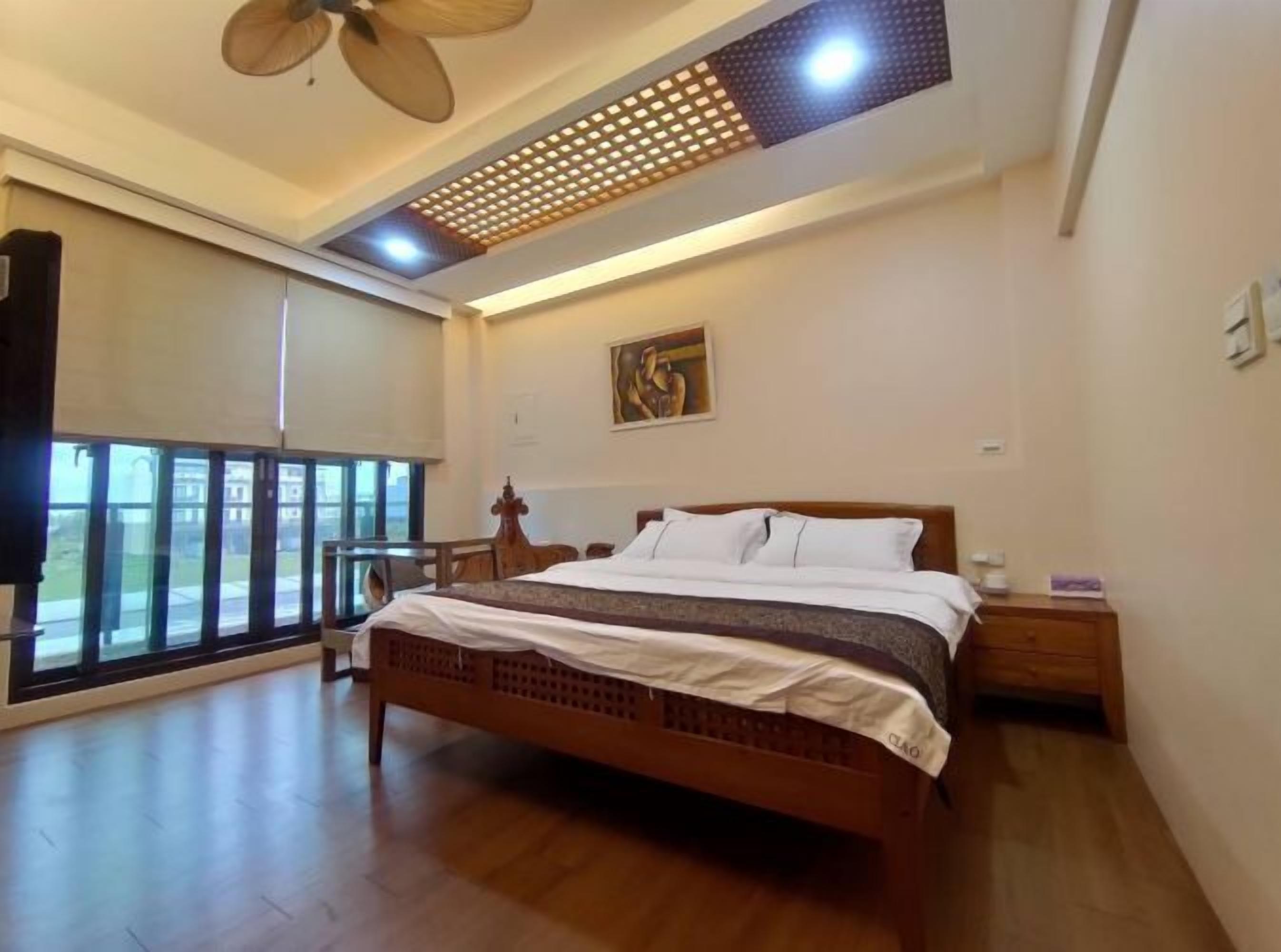 Un dormitorio con una cama grande, ventilador de techo, ventana con vistas y un cuadro en la pared.