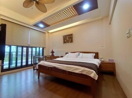 Un dormitorio con una cama grande, ventilador de techo, ventana con vistas y un cuadro en la pared.