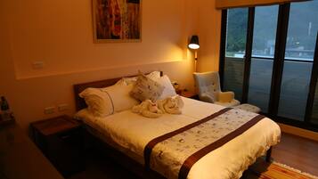 Habitación de hotel con una cama grande, una mesita de noche, una lámpara, una silla y una ventana con vistas al exterior.