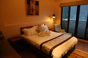 Habitación de hotel con una cama grande, una mesita de noche, una lámpara, una silla y una ventana con vistas al exterior.