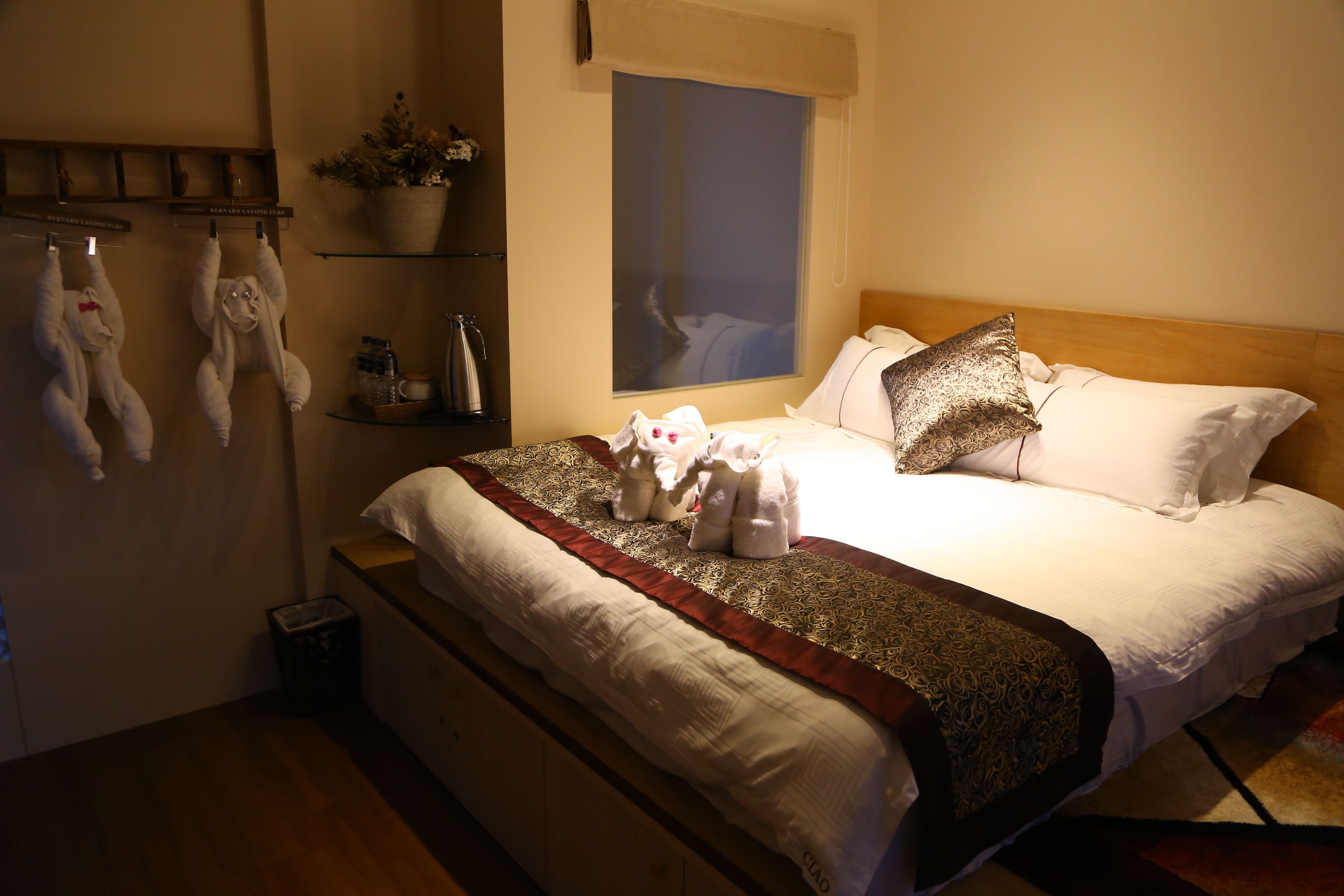 A neatly made bed with a patterned throw, a window with a view, and a shelf with toiletries.
