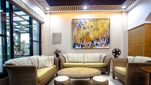Una sala de estar con muebles de mimbre, una mesa de centro redonda y un cuadro abstracto grande en la pared.