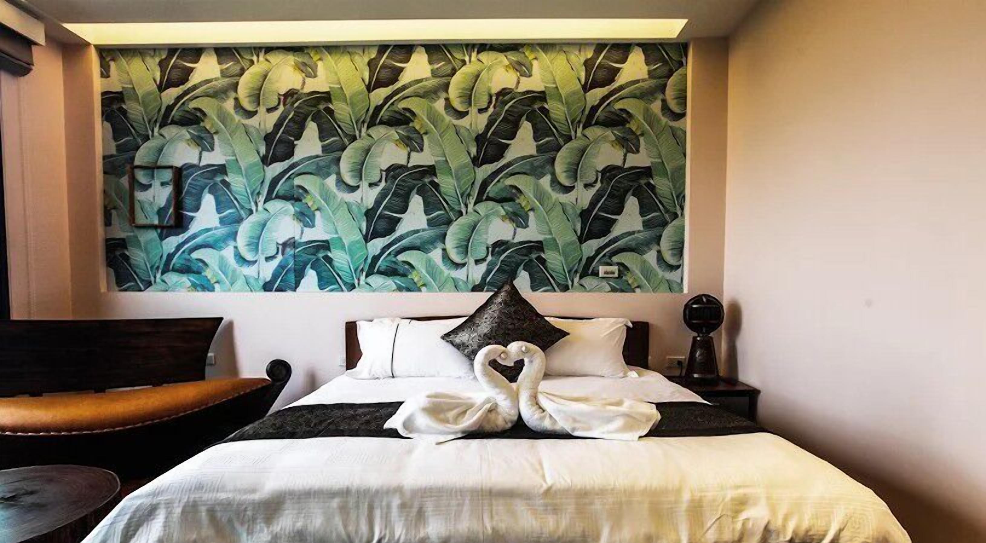 A hotel room with a bed, a heart-shaped pillow, a nightstand, a lamp, and a chair.