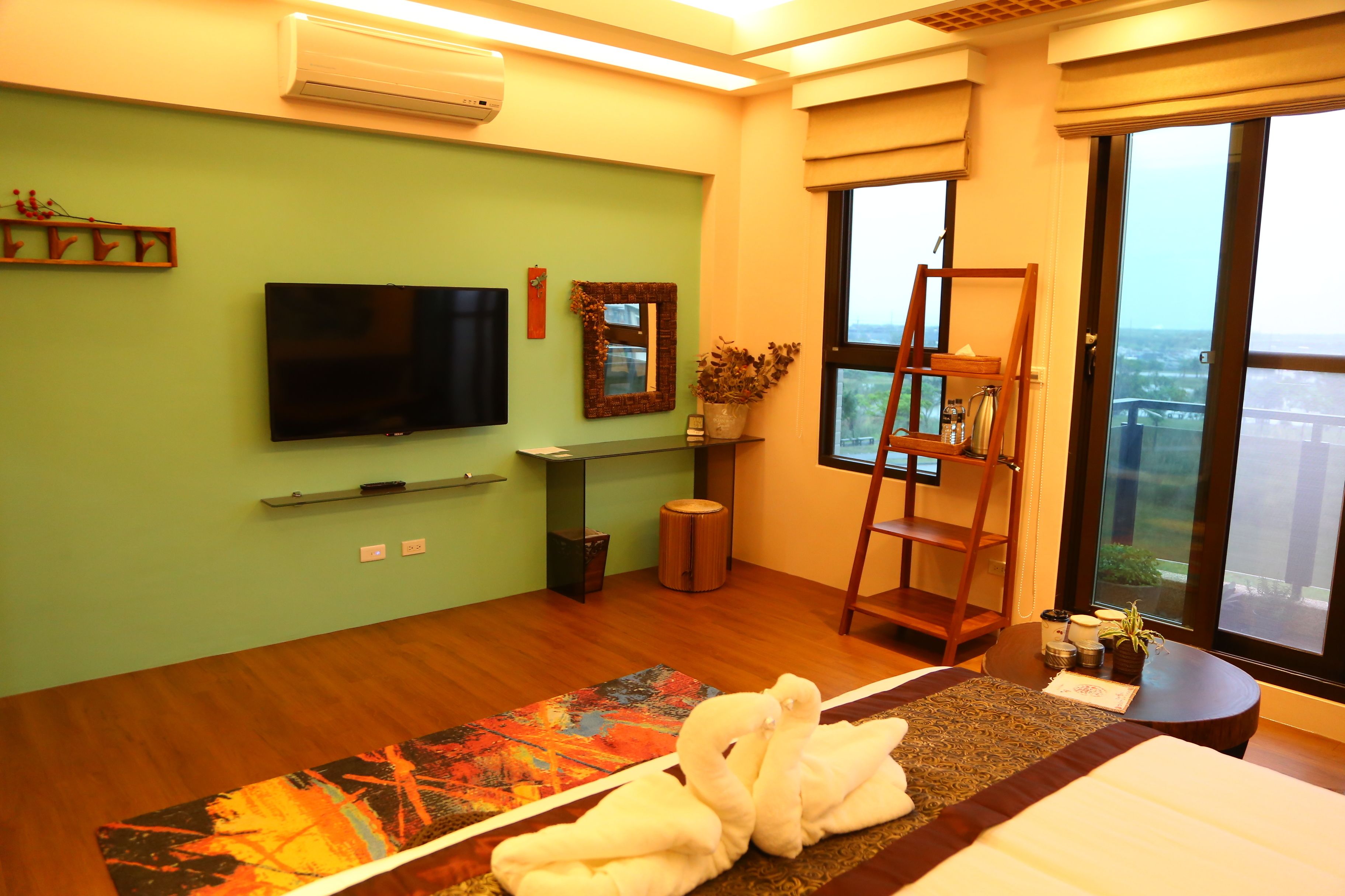 A modern hotel room with a large TV, a balcony with a view, and a wooden floor.
