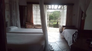 A room with two beds, a small table, and a chair. There is a window with curtains, and a view of greenery outside. - Jacaranda Lake Elementaita Lodge (Gilgil)