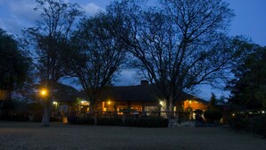 A two-story building with a patio area, surrounded by trees and a well-maintained lawn. - Jacaranda Lake Elementaita Lodge (Gilgil)