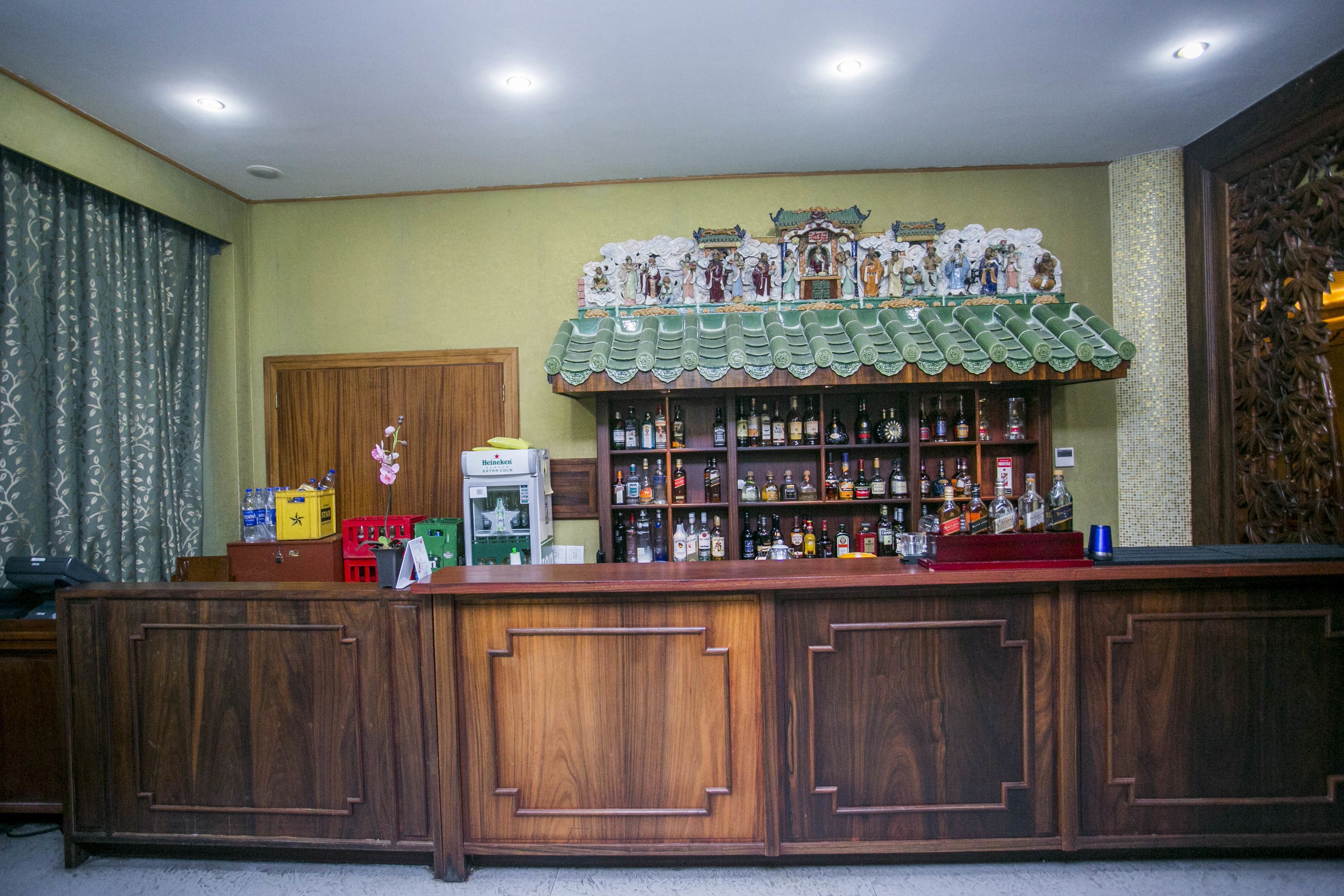 A bar area with wooden cabinets, shelves of liquor bottles, and a decorative ceiling.